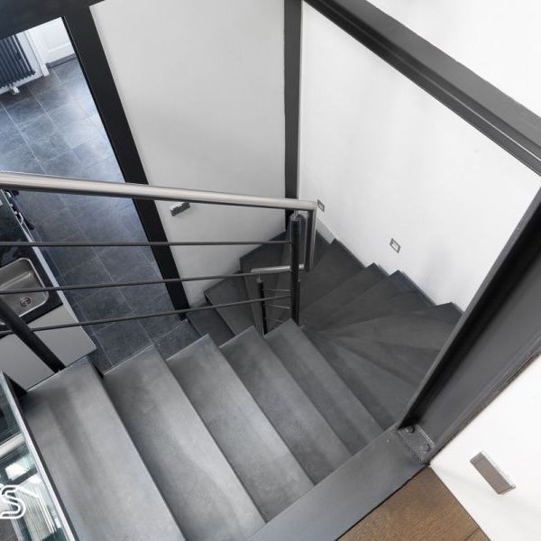 Trappen met metalen treden, glazen passerelle en inox handgreep. Een moderne trap op maat.